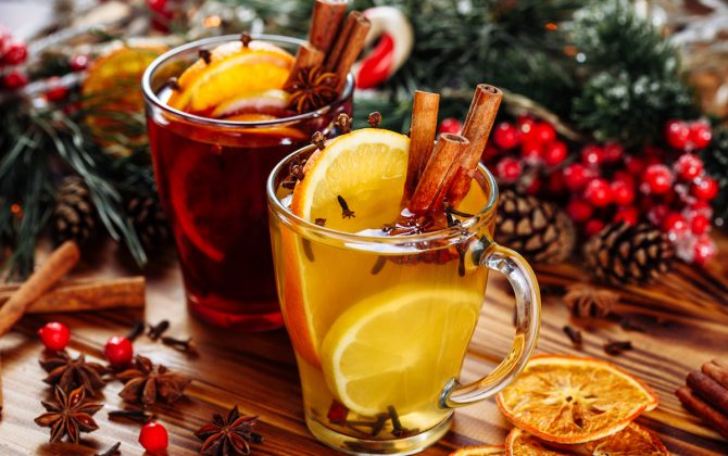 Two glasses of hot mulled wine with oranges and spices on wooden background. Close-up side view.
